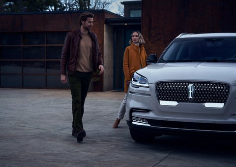 A man and a woman approaching a 2024 Lincoln Aviator® SUV, which illuminates certain lights when they are close | Brinson Lincoln of Corsicana in Corsicana TX